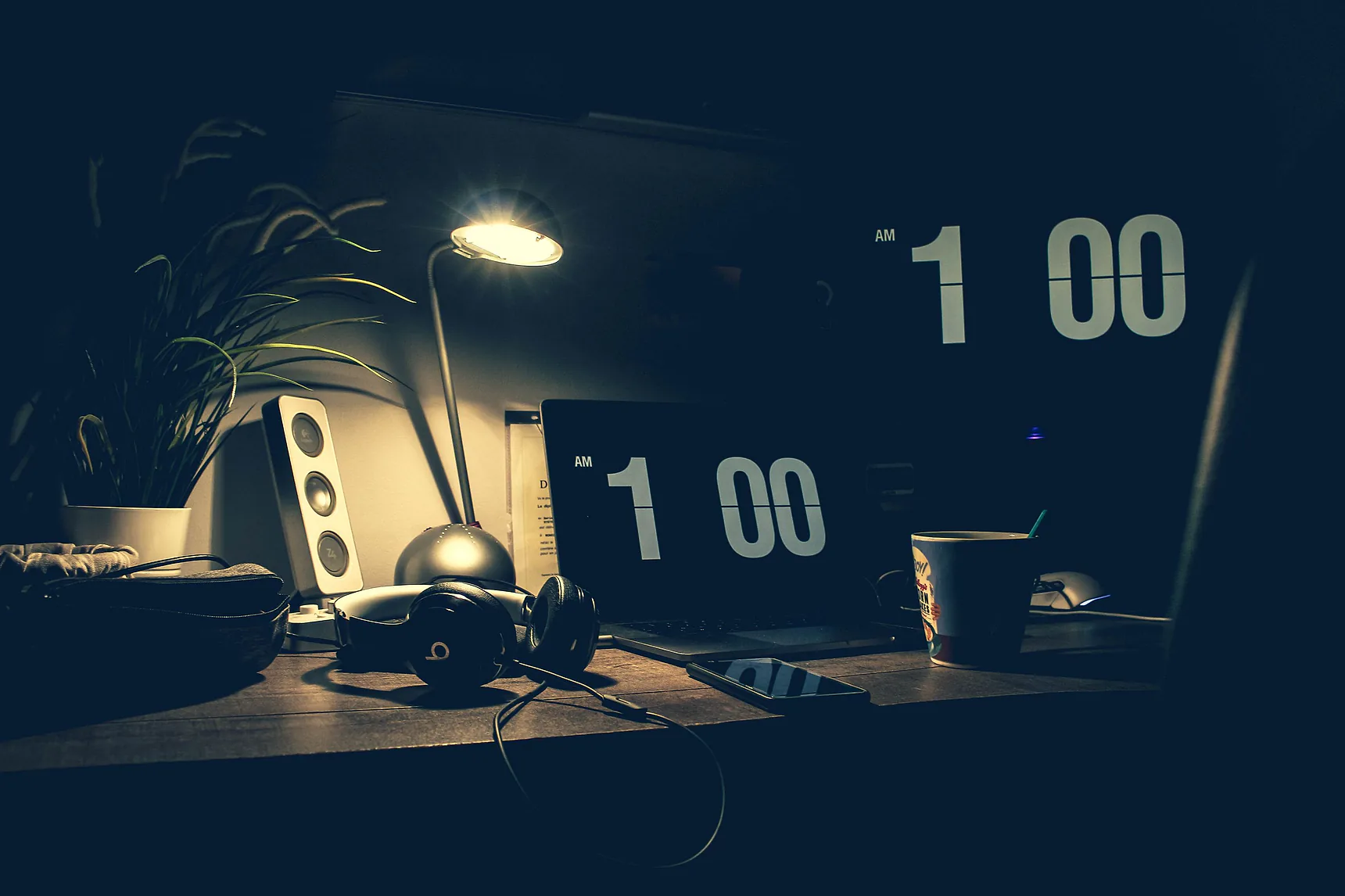 Desk at night lit by a lamp, with a clock showing 1:00 am and a phone