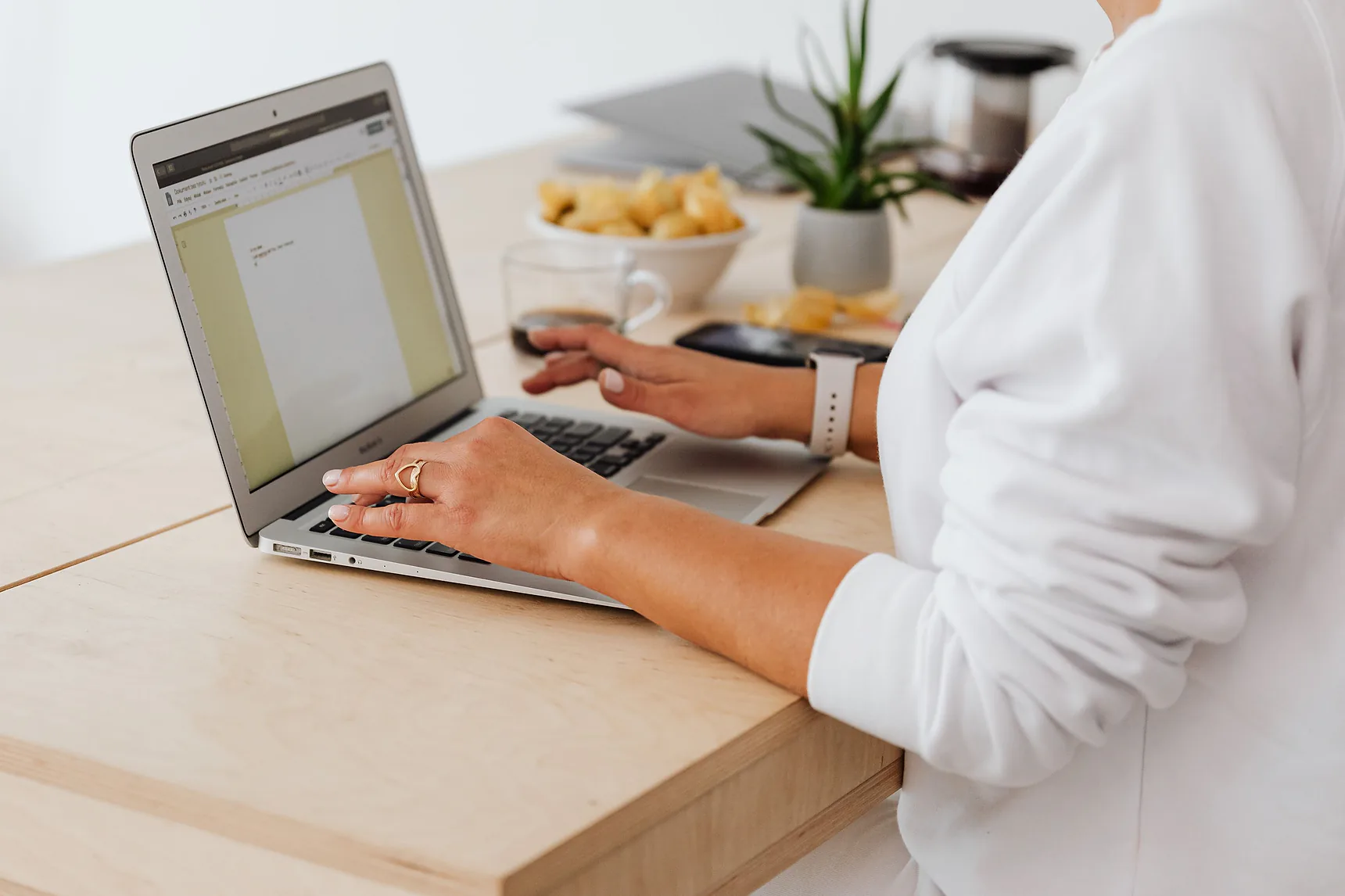 Person typing a document on a laptop at a bright wooden desk