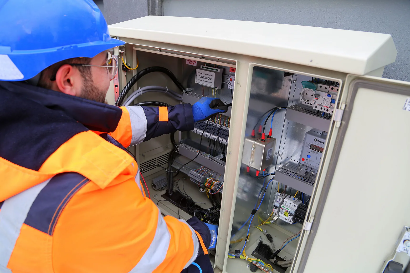 Electrician in a blue hard hat and hi-vis jacket working inside an electrical cabinet