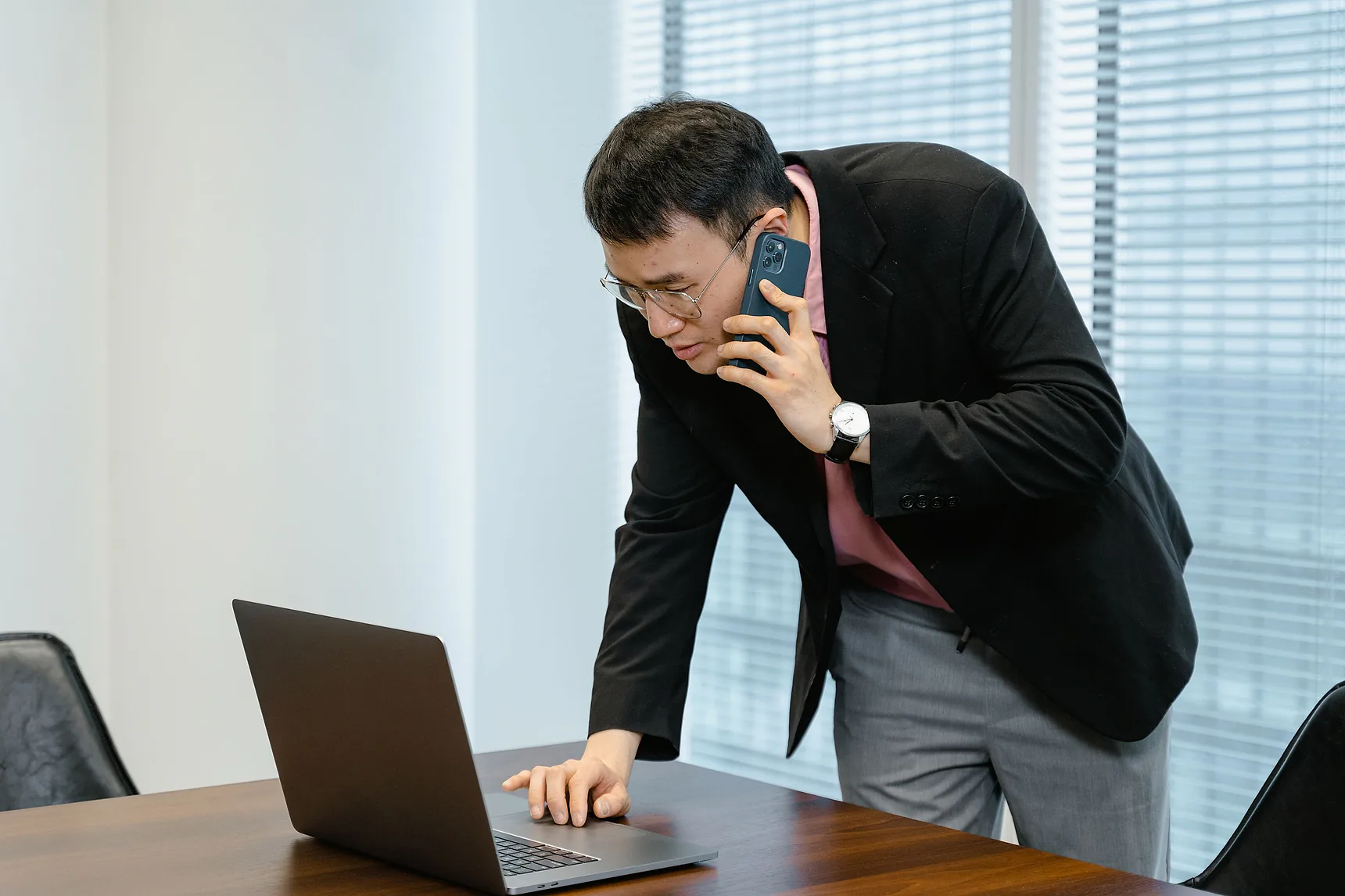 Man on a phone call leaning over a laptop at an office desk