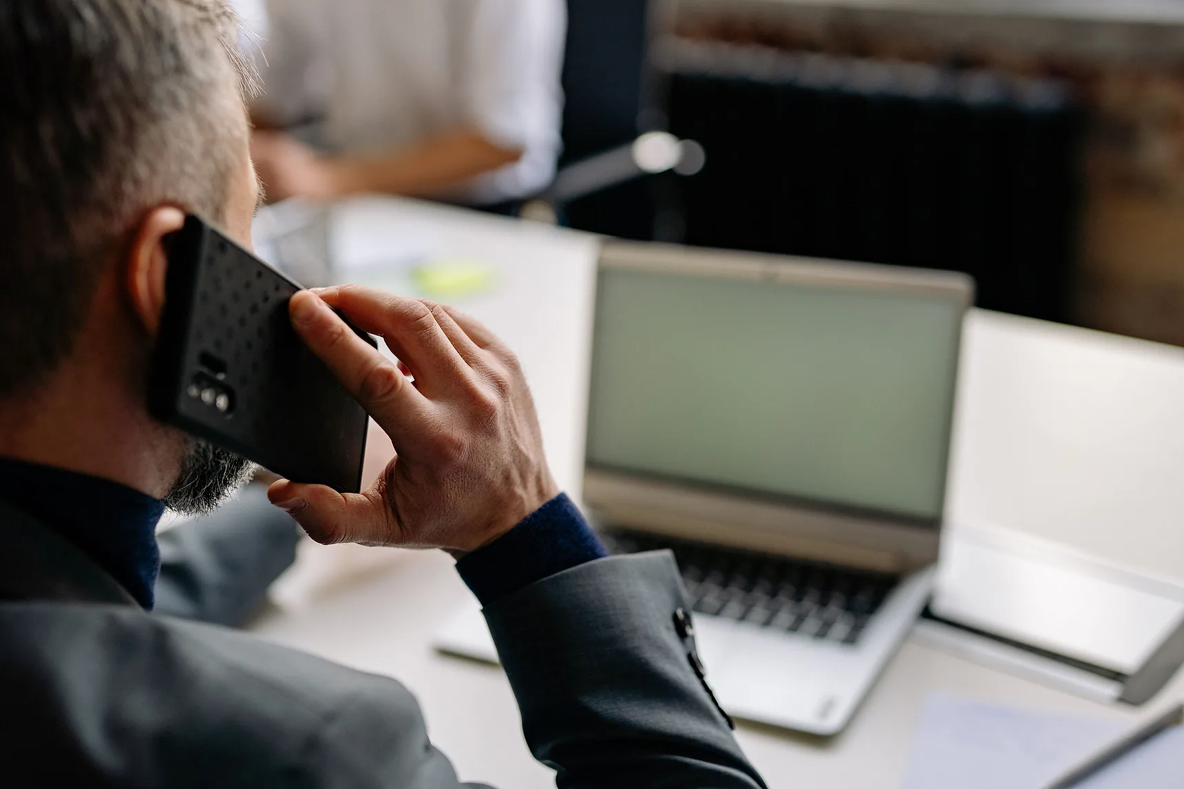 Man on a phone call at a desk beside an open laptop