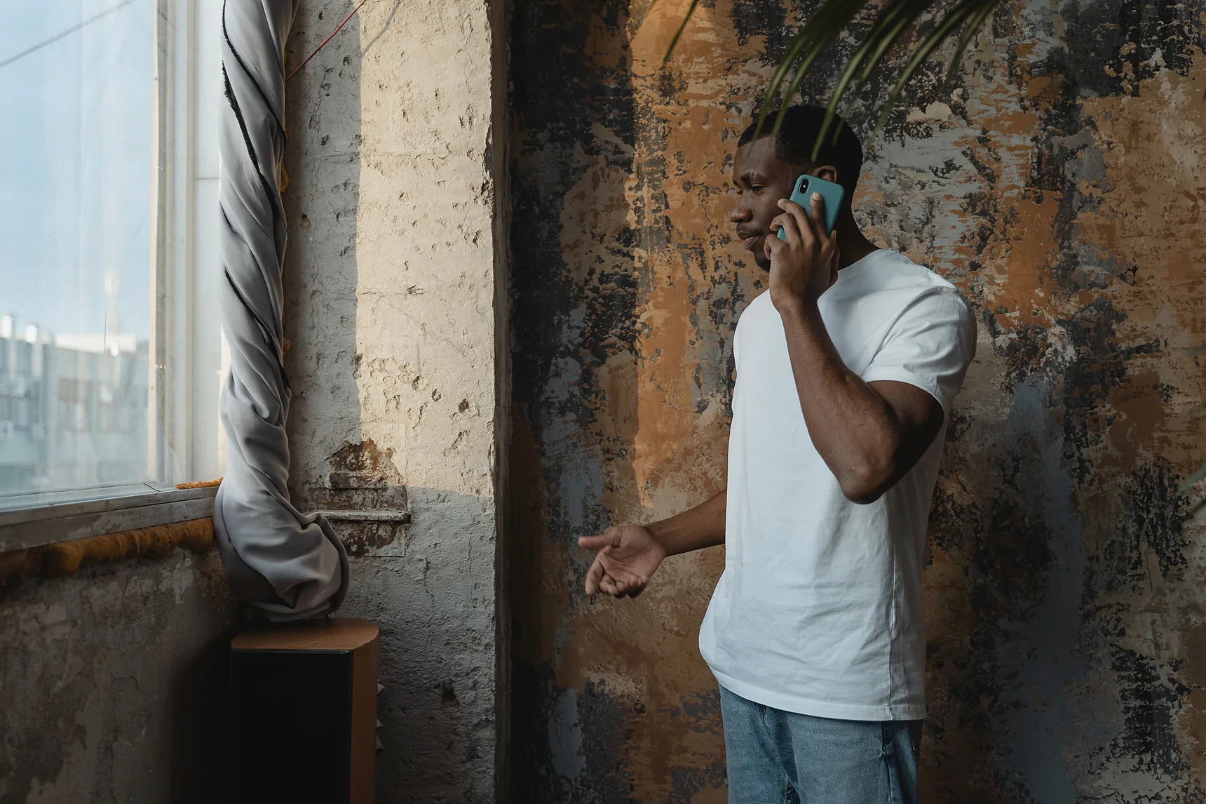 Man in a white T-shirt taking a phone call in a half-renovated room